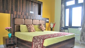 A bedroom with a wooden headboard, a bed with patterned pillows, a nightstand, a window with curtains, and a chair. - Billing Vista Guest House (Jogindarnagar)