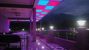 An outdoor dining area with tables and chairs, a ceiling with illuminated panels, and a view of mountains in the background. - Billing Vista Guest House (Jogindarnagar)