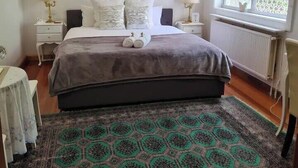 Un dormitori amb un llit gran, dues taules de nit amb làmpades, una finestra amb cortines estampades i una obra d'art emmarcada a la paret.