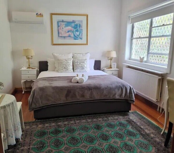 Un dormitorio con una cama grande, dos mesitas de noche con l ámparas, un ventanal con cortinas estampadas y una obra de arte enmarcada en la pared.