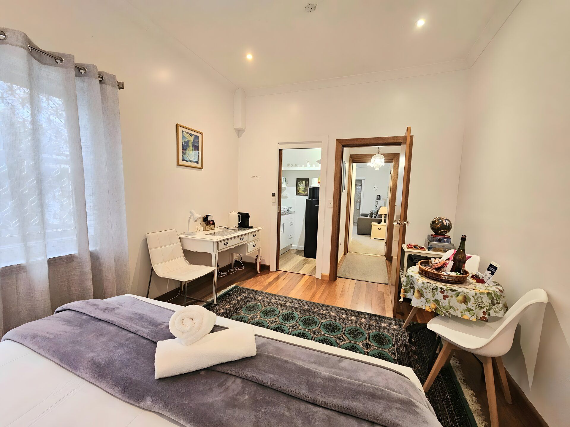 A hotel room with a bed, desk, chair, and a small table with a bottle and a bowl.