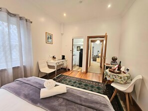 Une chambre d’hôtel avec un lit, un bureau, une chaise et une petite table sur laquelle se trouvent une bouteille et un bol.