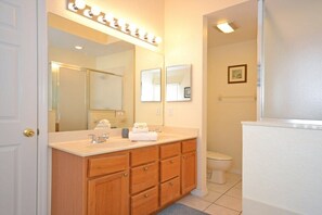 Une salle de bain avec un meuble-lavabo à deux vasques, un grand miroir avec éclairage intégré, des toilettes et un tableau encadré au mur.