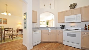 A kitchen with wooden cabinets, a white stove, and a microwave. There is a dining area with a table and chairs, and a chandelier. - Ffv8471ha - Highlands Reserve - 4 Bed 2 Baths Villa (Davenport)