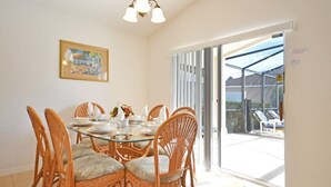 Uma sala de jantar com uma mesa de vidro rodeada por cadeiras de vime, um candelabro e um quadro na parede.