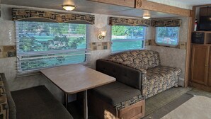 Ein gemütliches Wohnmobil-Interieur mit Essbereich, gepolsterten Sitzgelegenheiten und großen Fenstern mit Jalousien.