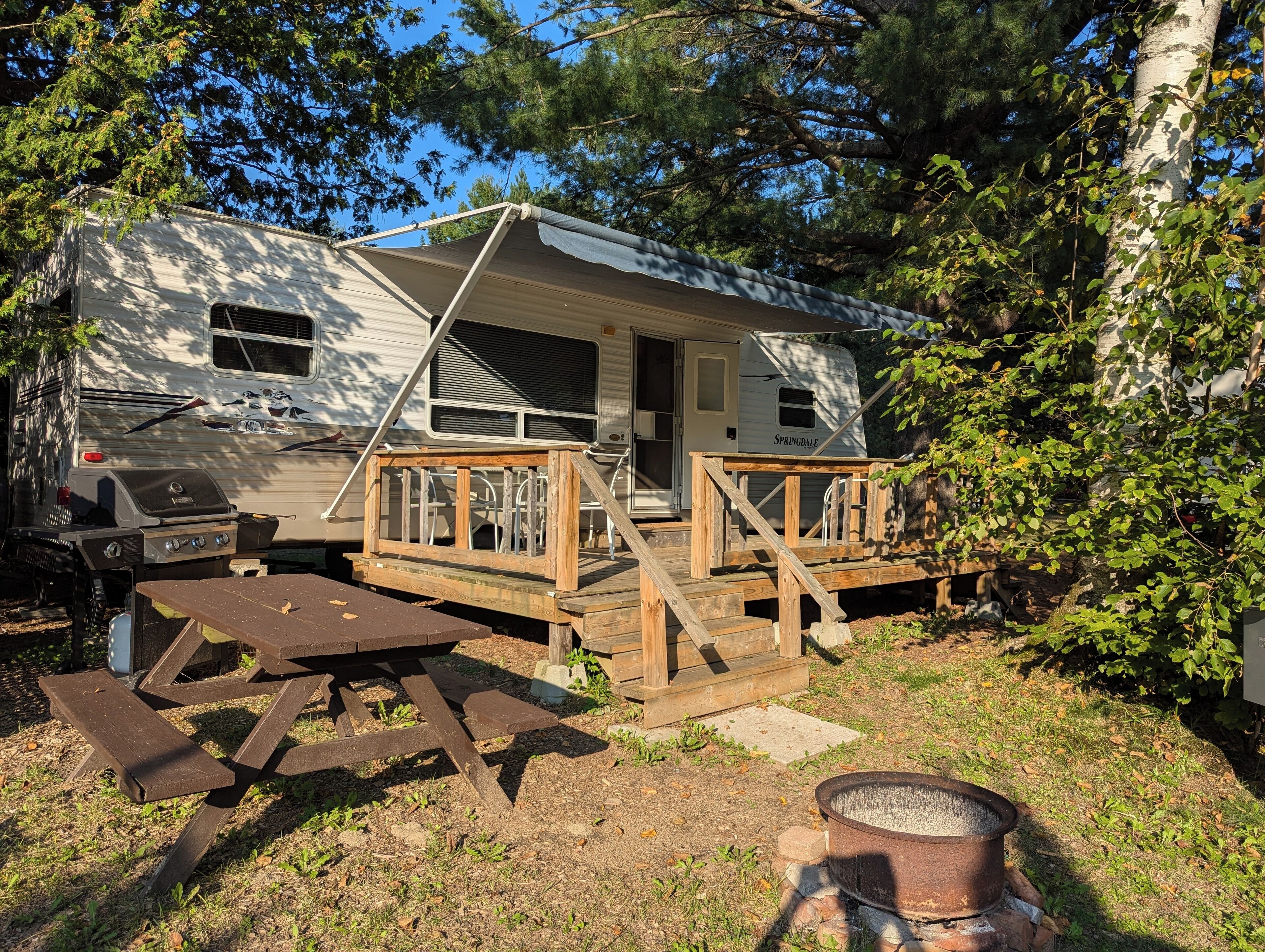 A mobile home with a covered porch, a picnic table, and a fire pit.