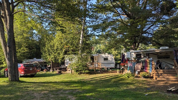 Ein Campingplatz mit Wohnmobilen, einem Picknicktisch und einem überdachten Bereich, an dem Wäsche hängt.
