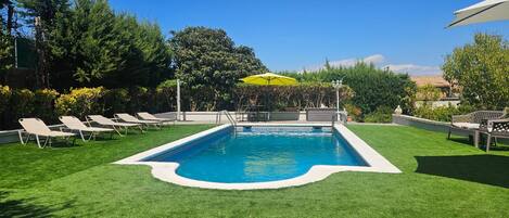Una piscina rectangular con borde blanco, rodeada de césped cuidado y sillas de descanso.