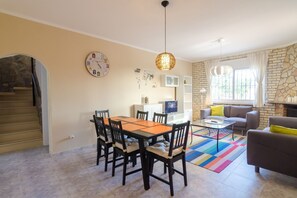 A dining area with a table and chairs, a TV, and a fireplace in a living room with a stone wall and a staircase.