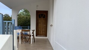 A staircase leading to a wooden door with a window, a table with chairs, and a blue fence in the background. - WONDERFUL CALALIBEROTTO (Sos Alinos)