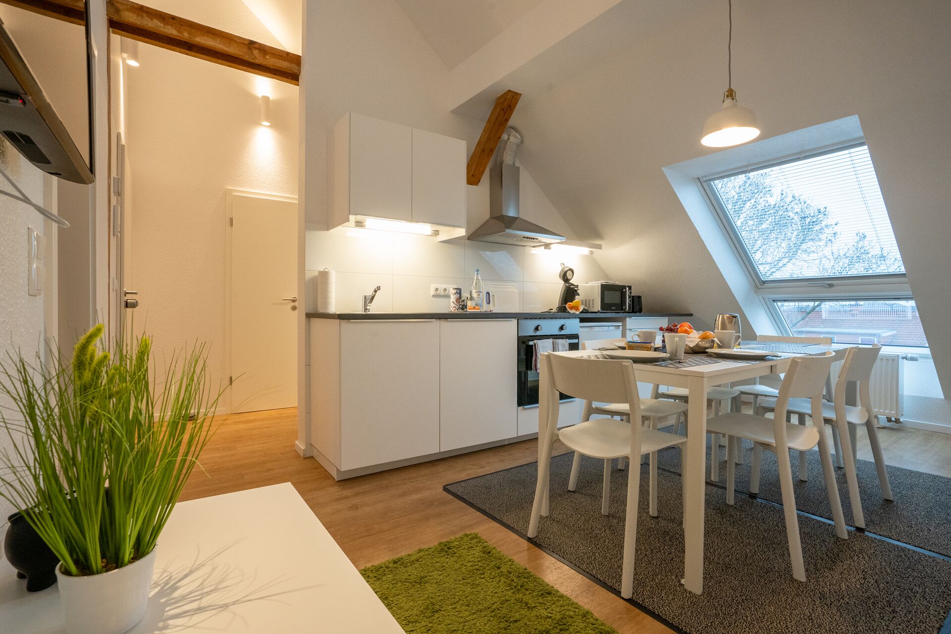 A modern kitchen with white cabinets, a dining table with chairs, a small oven, and a window with a view of trees.