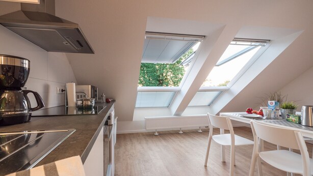 A modern kitchen with a coffee maker, a kettle, and a dining area with a table and chairs. - Meine Zeitwohnung (Essen)