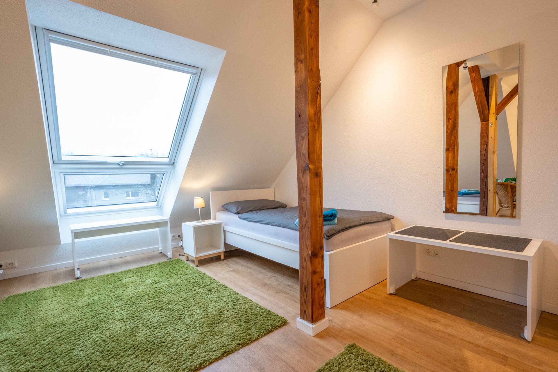 Un dormitorio moderno con tragaluces, una cama, una mesita de noche, un espejo y una alfombra verde.