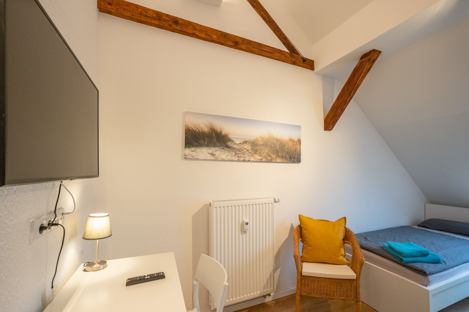 Une pièce confortable avec un lit, une chaise, une table avec une lampe, un tableau et un radiateur.