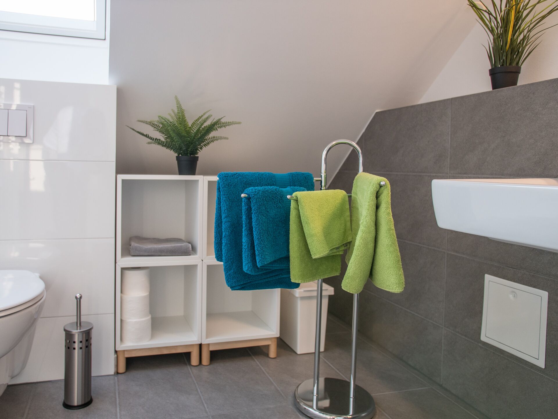 Une salle de bain avec un lavabo blanc, un porte-serviettes avec des serviettes bleues et vertes, une plante en pot et des toilettes.