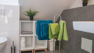 Une salle de bain avec un lavabo blanc, un porte-serviettes avec des serviettes bleues et vertes, une plante en pot et des toilettes.