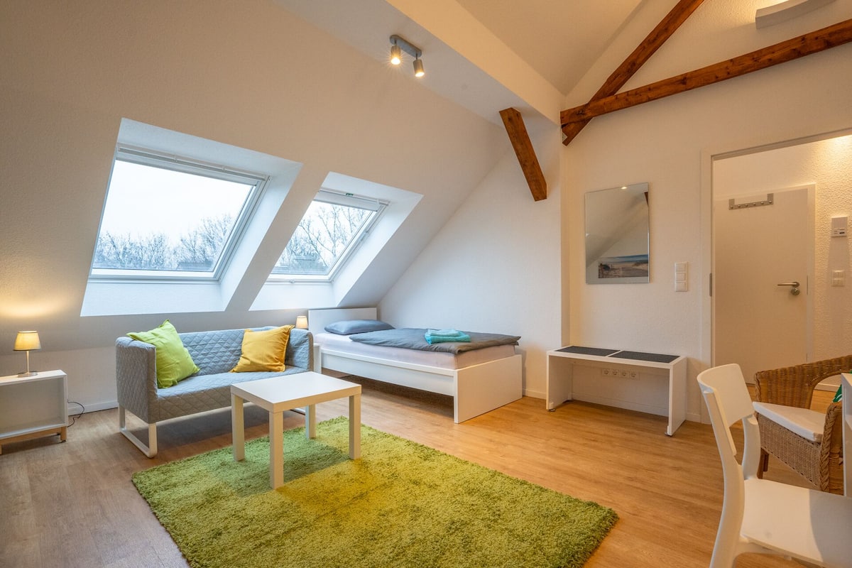 A modern loft bedroom with skylights, a bed, a desk, and a seating area.