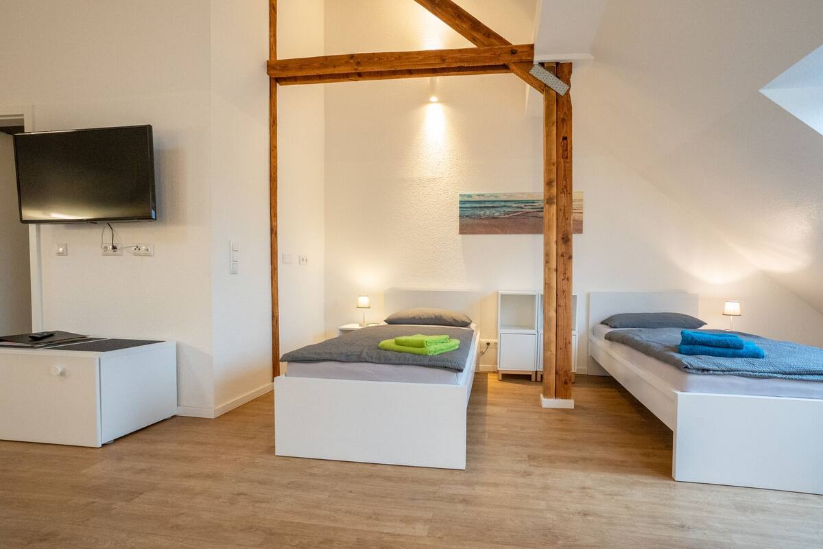 A modern, well-lit room with a loft bed, a flat-screen TV, and a small desk.