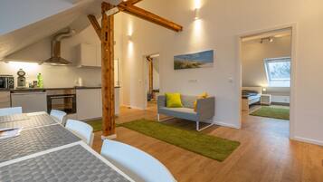 A modern interior with a dining area, kitchen, and living space featuring wooden beams, a painting, and a view through a window.