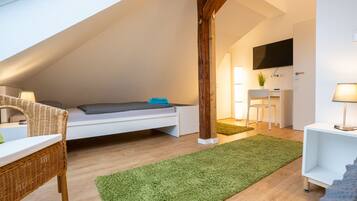 Une chambre à coucher aménagée en mezzanine, avec un plafond en pente, un lit, un bureau, une chaise et un téléviseur fixé au mur.