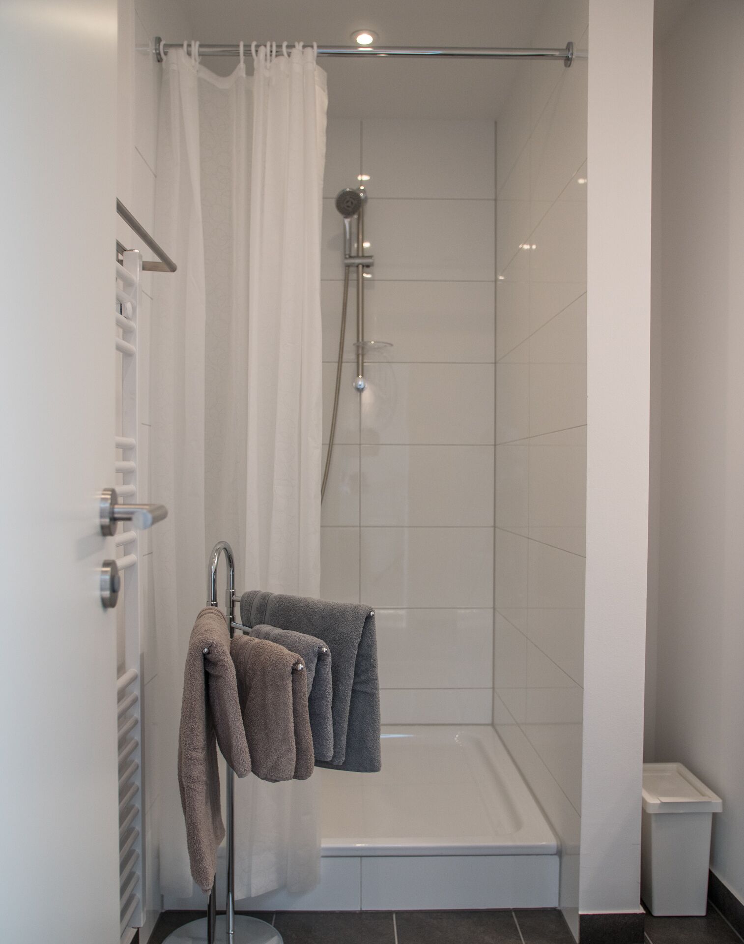 Um chuveiro com porta de vidro, um porta-toalhas com duas toalhas e um vaso sanitário branco num banheiro.