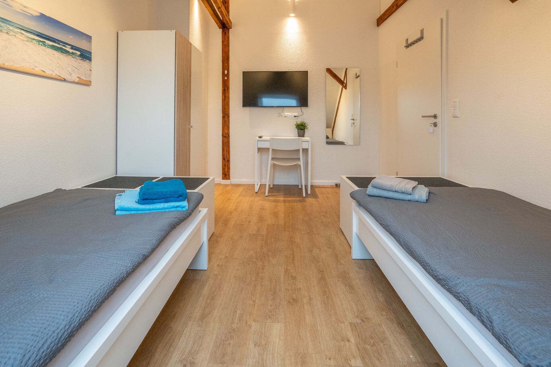 A room with two single beds, a desk, a chair, a TV, and a door.