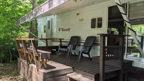 Een overdekt terras met houten banken en stoelen, een picknicktafel, en een kleine trap naar een overdekte ruimte.