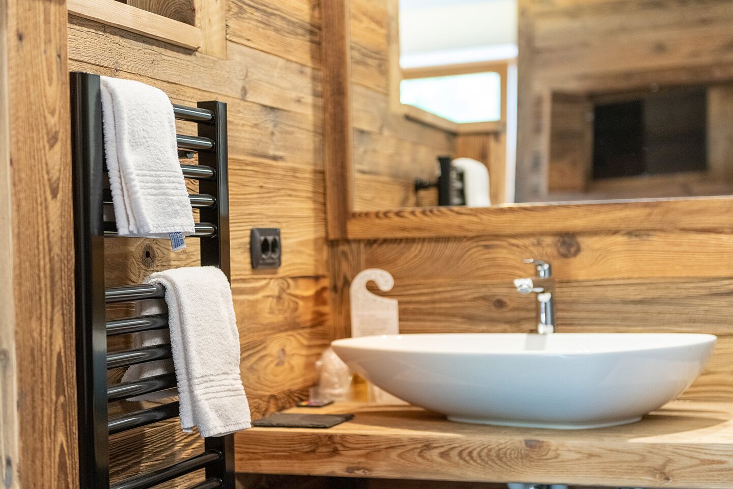 Ein Badezimmer mit Holzwand, einem schwarzen Handtuchhalter und weißen Handtüchern sowie einem weißen Waschbecken.