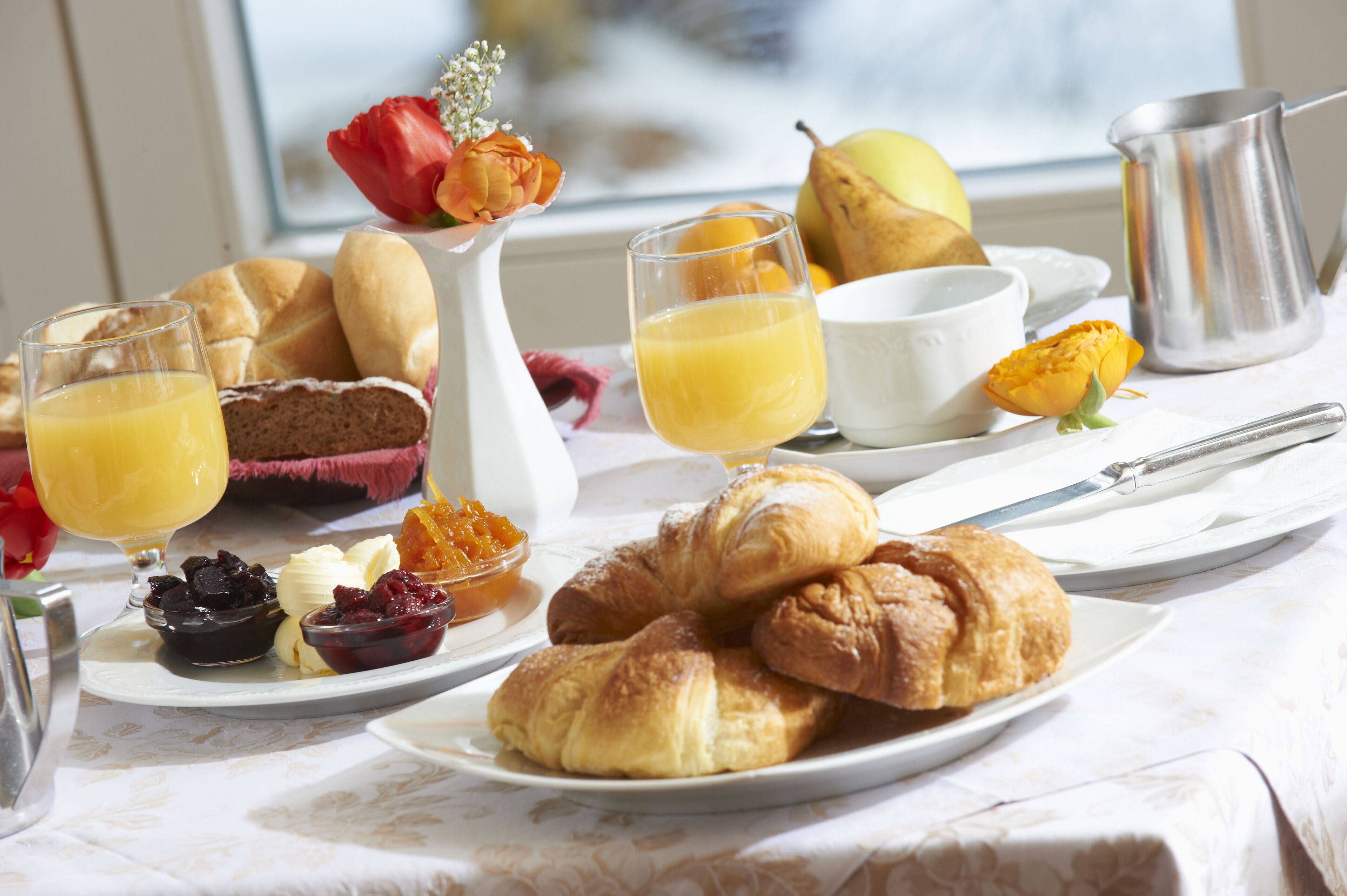 En frukostuppdukning med croissanter, frukt och juice på ett bord.