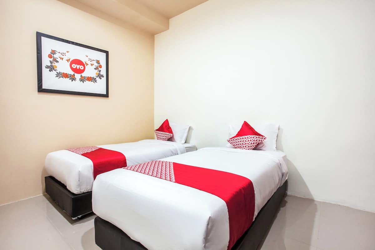 Ein Hotelzimmer mit zwei Betten, jeweils mit weißer und roter Bettwäsche, und einem gerahmten Bild an der Wand.
