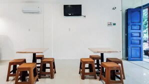 A room with two tables and four stools, a flat-screen TV mounted on the wall, and a blue door leading outside. - Hotel O Palem Mas Garden (Medan)