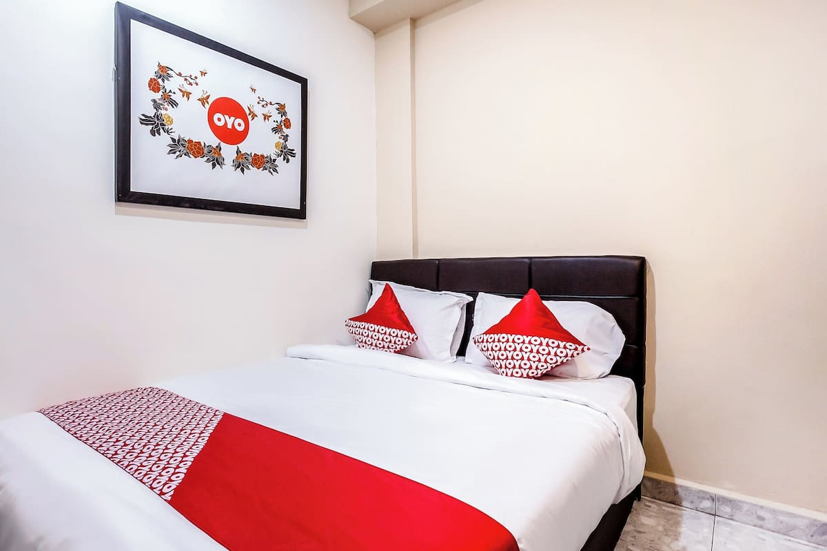 Ein ordentlich gemachtes Bett mit einer weißen und roten Bettdecke, zwei Kissen mit rotem und weißem Muster und ein gerahmtes Bild mit floralem Dekor und dem Schriftzug „OYO“ an der Wand.