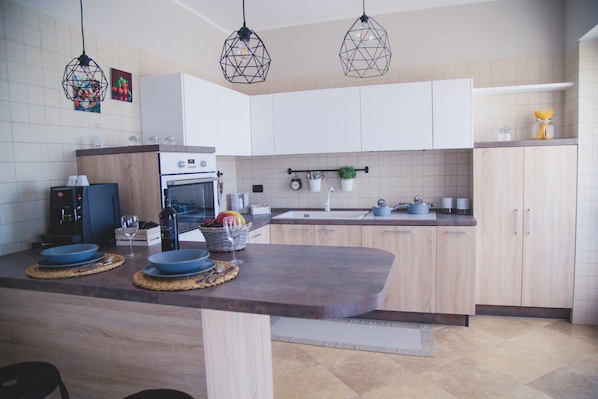 A modern kitchen with a central island, white cabinets, and hanging pendant lights.