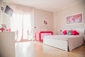 A bedroom with a bed, a desk, a chair, a TV, and a window with curtains.