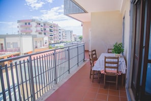 A balcony with a table and chairs, a potted plant, and a view of neighboring buildings.