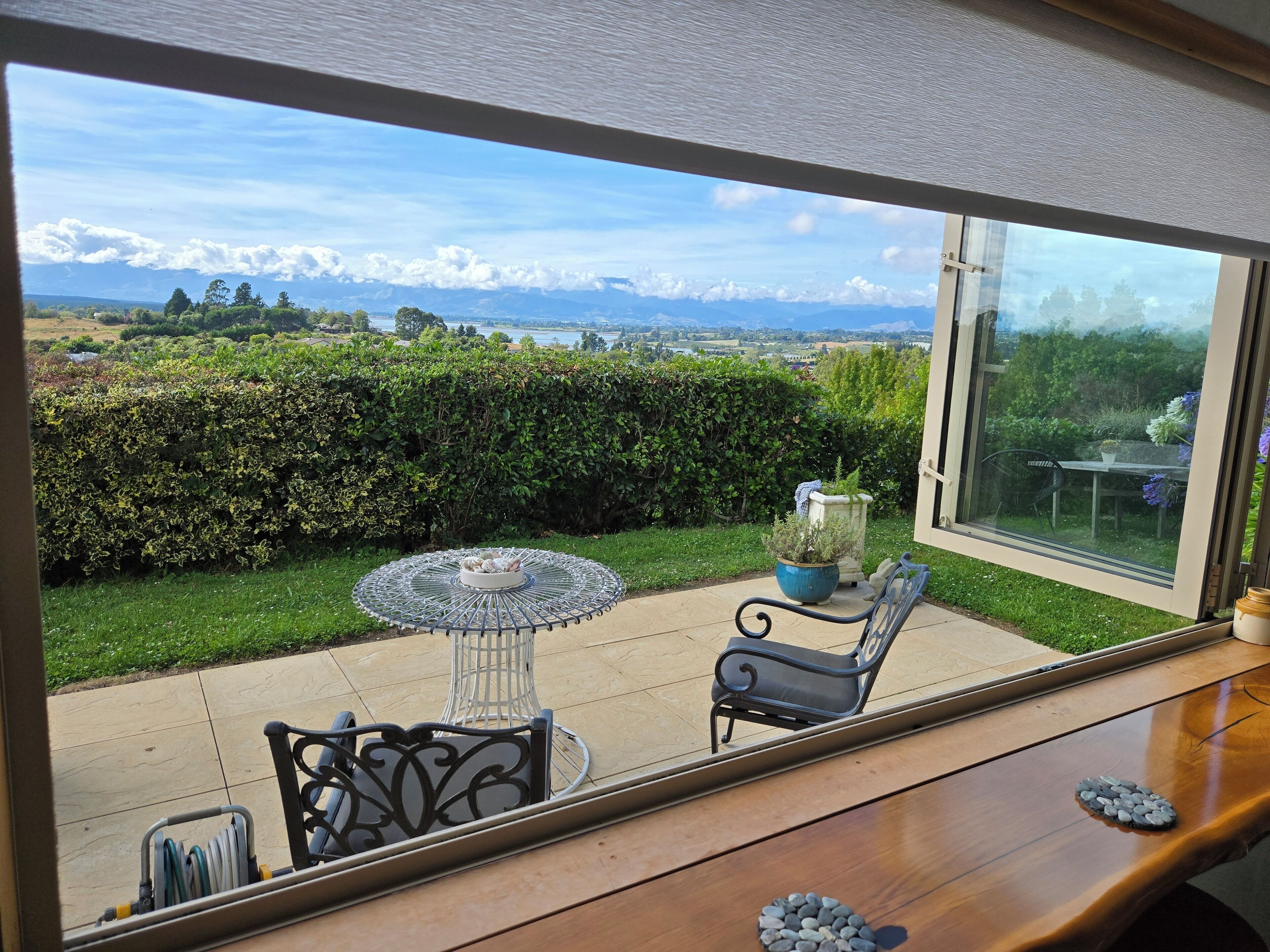 A patio with a table and chairs, a large window with a view of mountains and greenery.