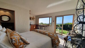 Ein Schlafzimmer mit einem großen Bett, einer kleinen Küchenzeile und Blick ins Freie.