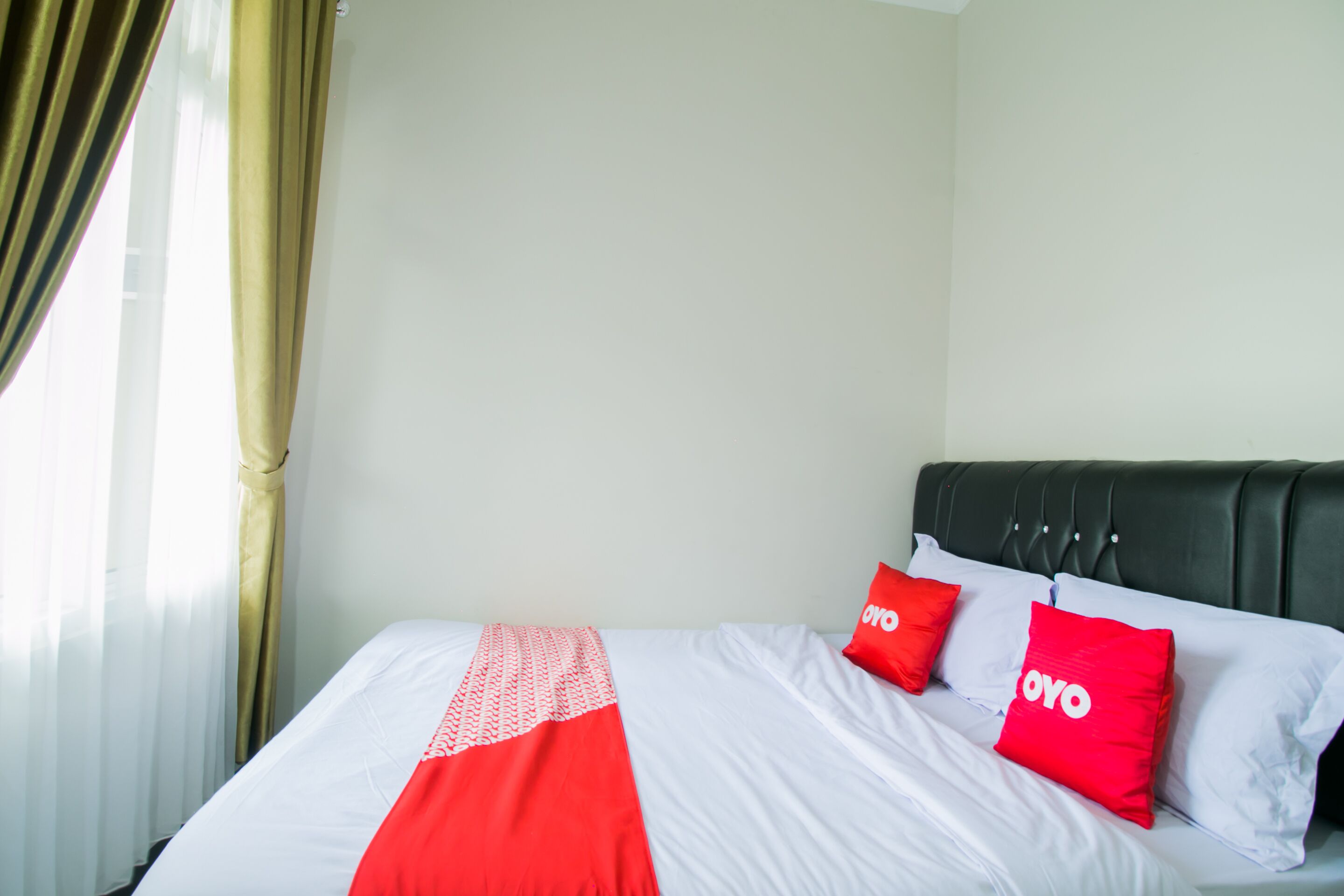 A bed with white and red bedding, two red pillows with the word "OYO" on them, and a black headboard.