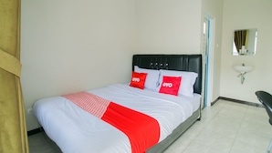 Una cama bien hecha con una colcha blanca y roja, un cabecero negro y dos almohadas con la palabra 'OYO' en ellas.