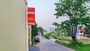 Calle residencial con un letrero rojo que anuncia una propiedad en venta.