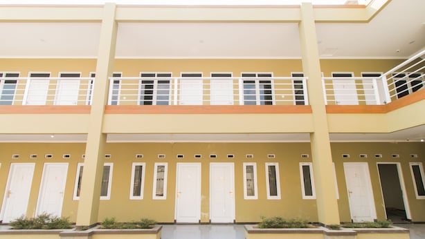 Un edificio de varios pisos con fachada amarilla, puertas blancas y un patio central con jardineras.