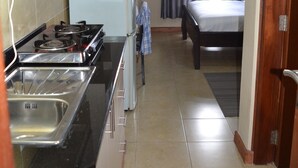 Eine kompakte Küche mit Herd, Spüle und Schränken, die in ein Schlafzimmer mit Bett und Vorhängen übergeht.
