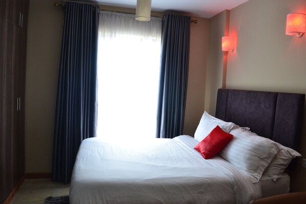 Une chambre d’hôtel avec un grand lit, des rideaux épais, une tête de lit et des lampes fixées au mur.