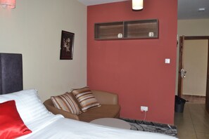 Une chambre d’hôtel avec un lit, une chaise, un mur rouge, un tableau encadré et une porte.