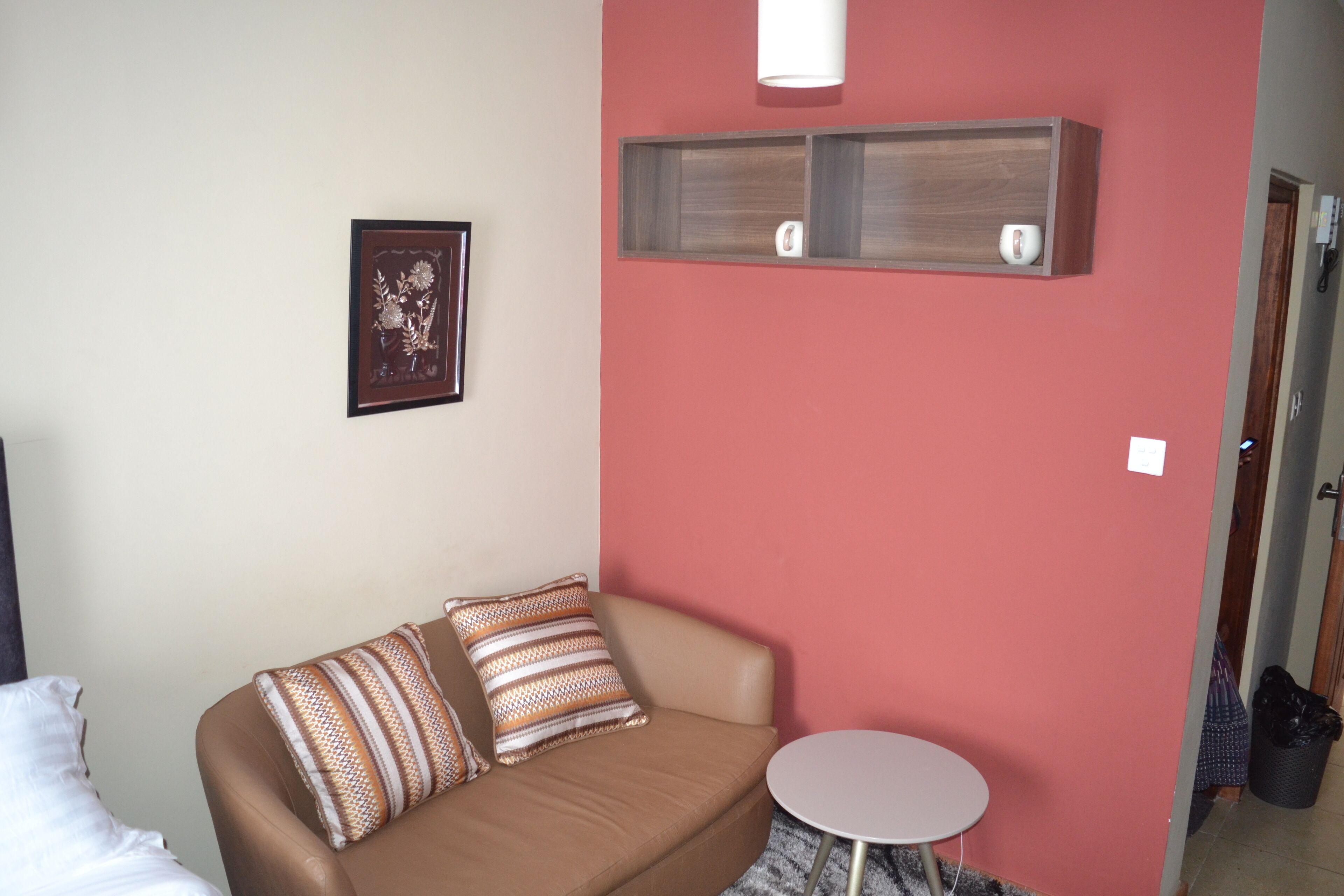 Una stanza con un divano marrone, un tavolino rotondo, un quadro appeso al muro e una mensola in legno con un pacchetto di fazzoletti.