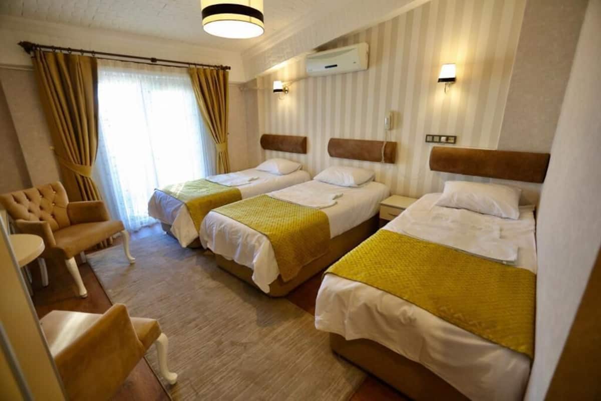 A hotel room with two single beds, a sofa, a small table, and an air conditioning unit on the wall.