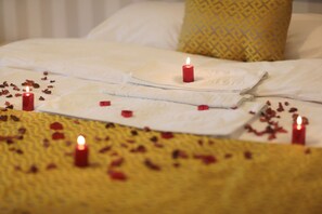A bed with white linens, a yellow patterned pillow, and red candles.