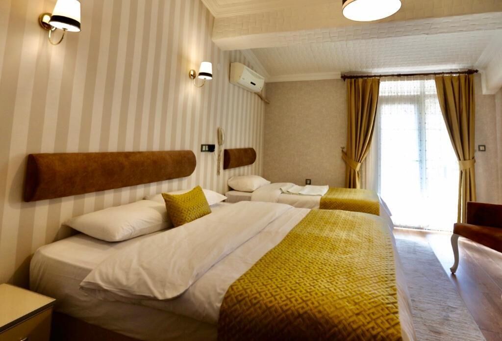 A hotel room with two beds, striped wallpaper, and a large window with curtains.