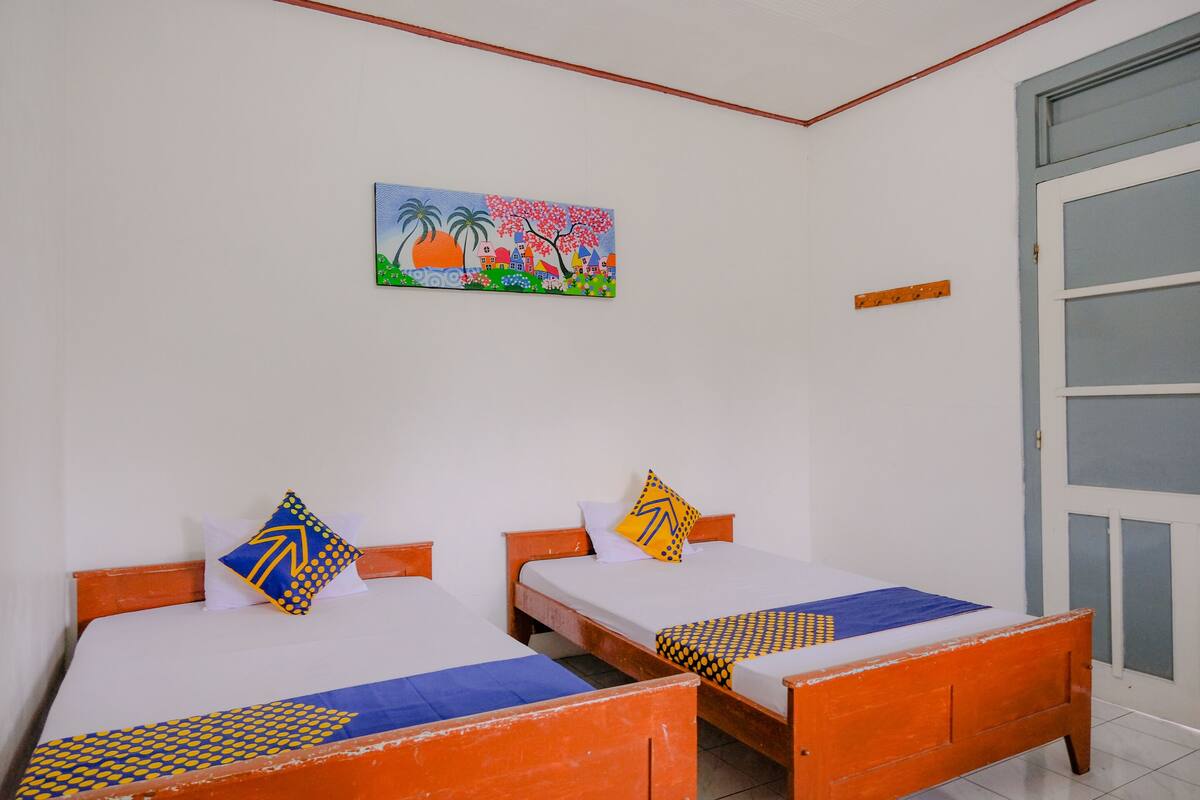 Ein Zimmer mit zwei Holzbettgestellen, weißen Wänden und einem farbenfrohen Bild an der Wand.